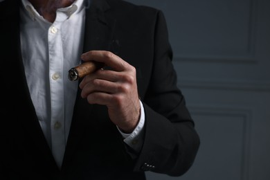 Man smoking cigar on dark grey background, closeup. Space for text