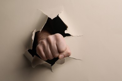 Photo of Man breaking through beige paper with fist, closeup