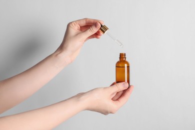 Photo of Woman holding bottle of cosmetic oil on light background, closeup