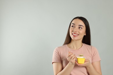 Photo of Happy woman with tasty yogurt on grey background. Space for text