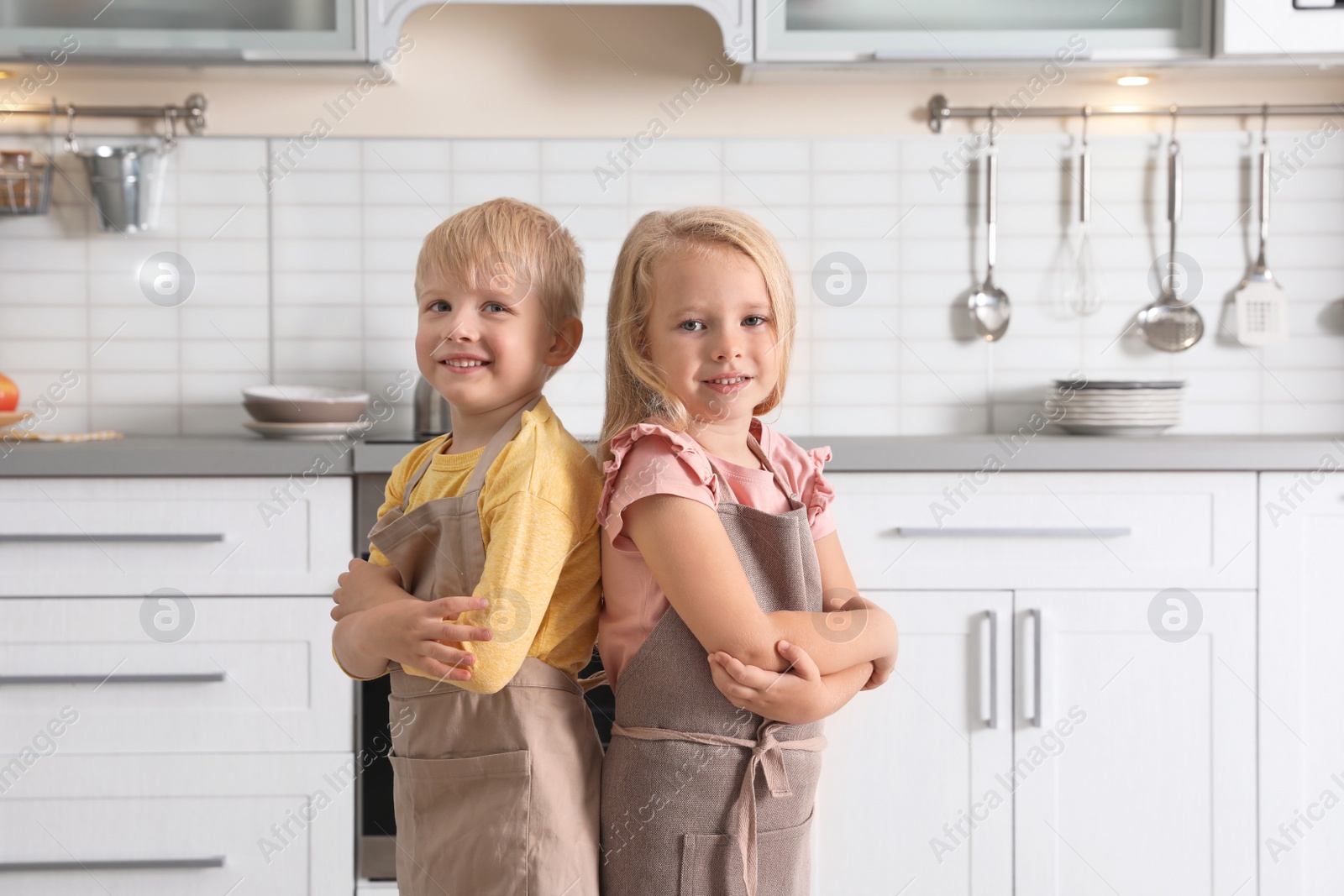 Photo of Cute little kids wearing aprons in kitchen