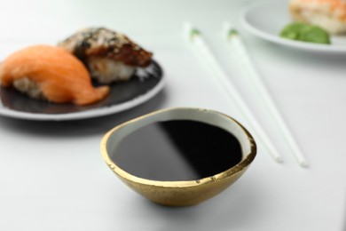 Tasty soy sauce in bowl, sushi and chopsticks on white marble table, closeup