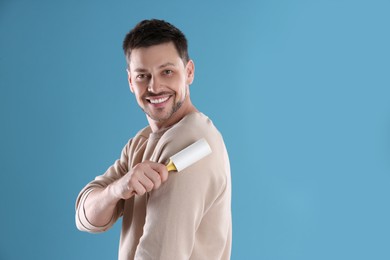 Man cleaning clothes with lint roller on light blue background. Space for text