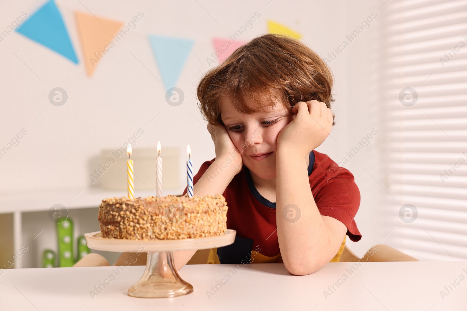 Photo of Cute boy with birthday cake at table indoors