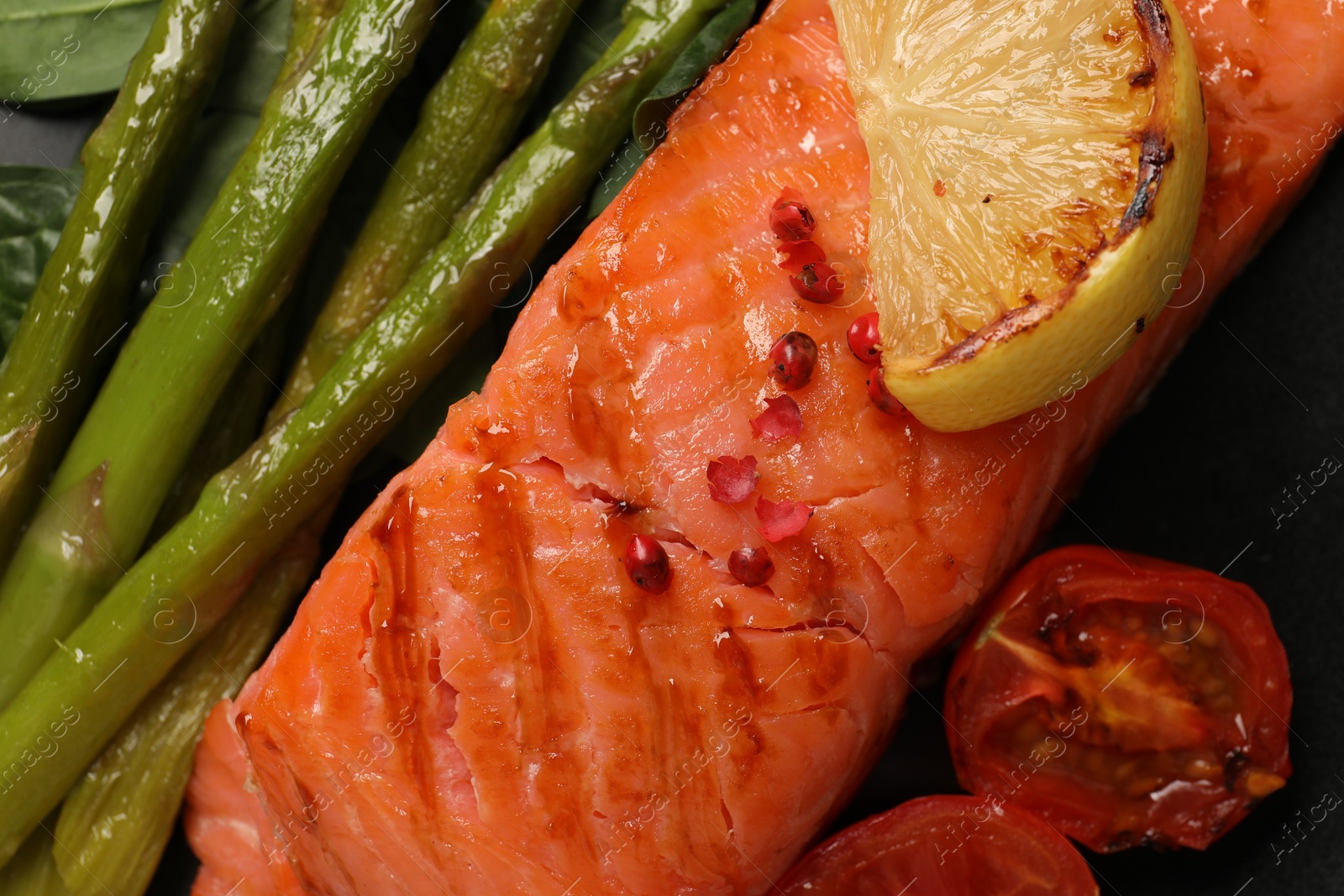 Photo of Plate with tasty grilled salmon, tomatoes, lemon and asparagus, top view