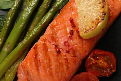 Photo of Plate with tasty grilled salmon, tomatoes, lemon and asparagus, top view