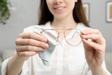 Photo of Woman cleaning glasses with microfiber cloth indoors, closeup