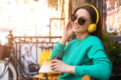 Happy young woman with coffee and headphones listening to music outdoors