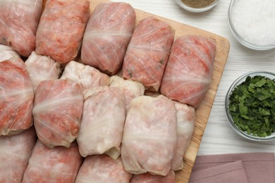 Uncooked stuffed cabbage rolls on white wooden table, flat lay