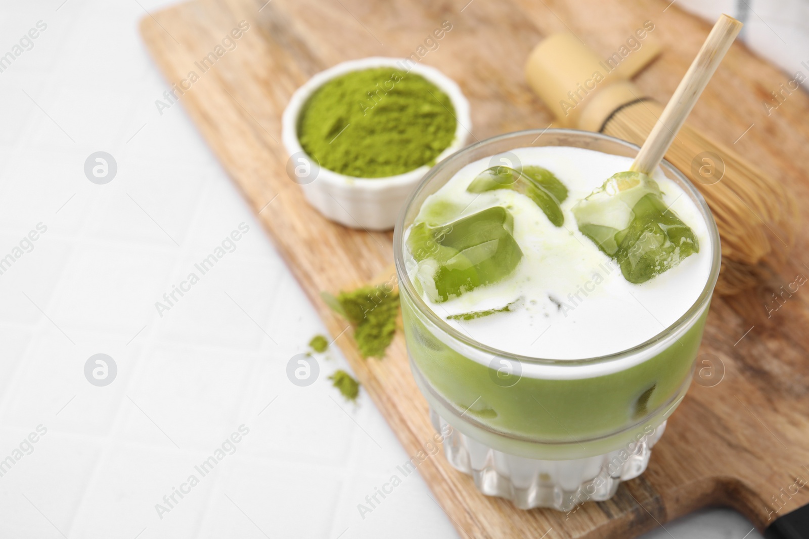 Photo of Glass of tasty iced matcha latte and powder on white tiled table. Space for text