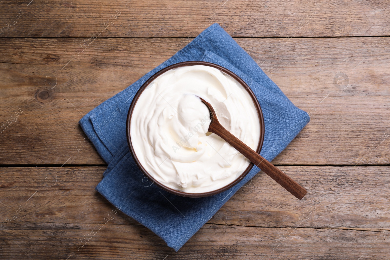 Photo of Top view of clay bowl with sour cream and spoon on wooden table