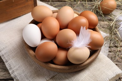 Photo of Fresh chicken eggs in bowl and dried hay on wooden table