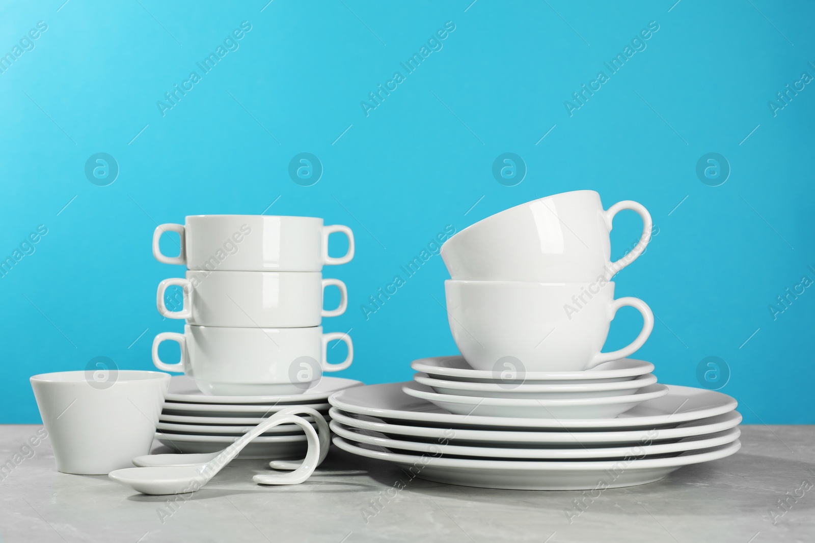 Photo of Set of clean dishware on grey table against light blue background