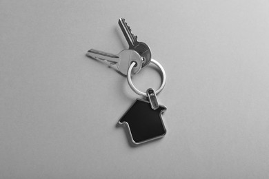 Keys with trinket in shape of house on grey background, top view. Real estate agent services
