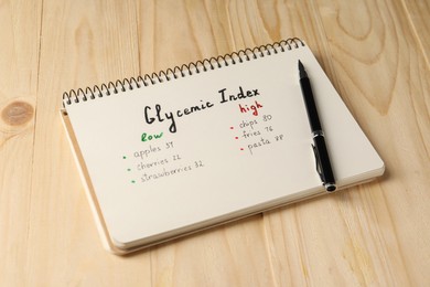 Photo of List with products of low and high glycemic index in notebook and pen on wooden table