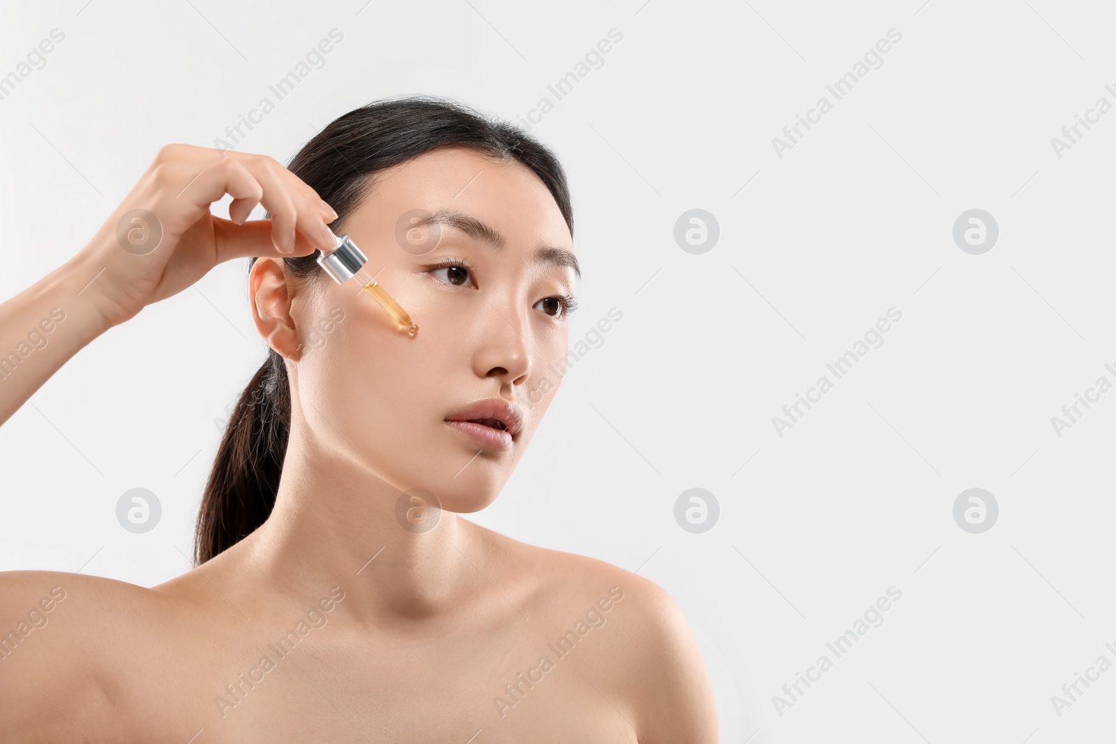 Photo of Beautiful young woman applying cosmetic serum onto her face on white background, space for text