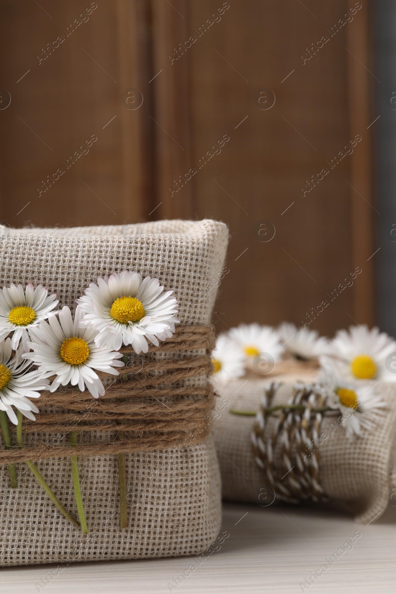 Photo of Gifts packed in burlap fabric, beautiful chamomiles, and ropes on white table, closeup