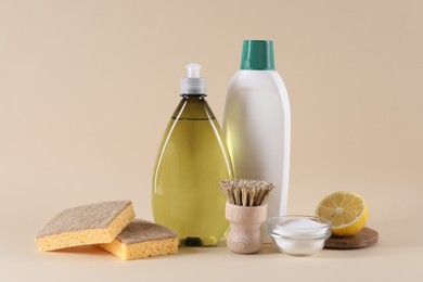 Bottles of cleaning product, brush, sponges, lemon and baking soda on beige background