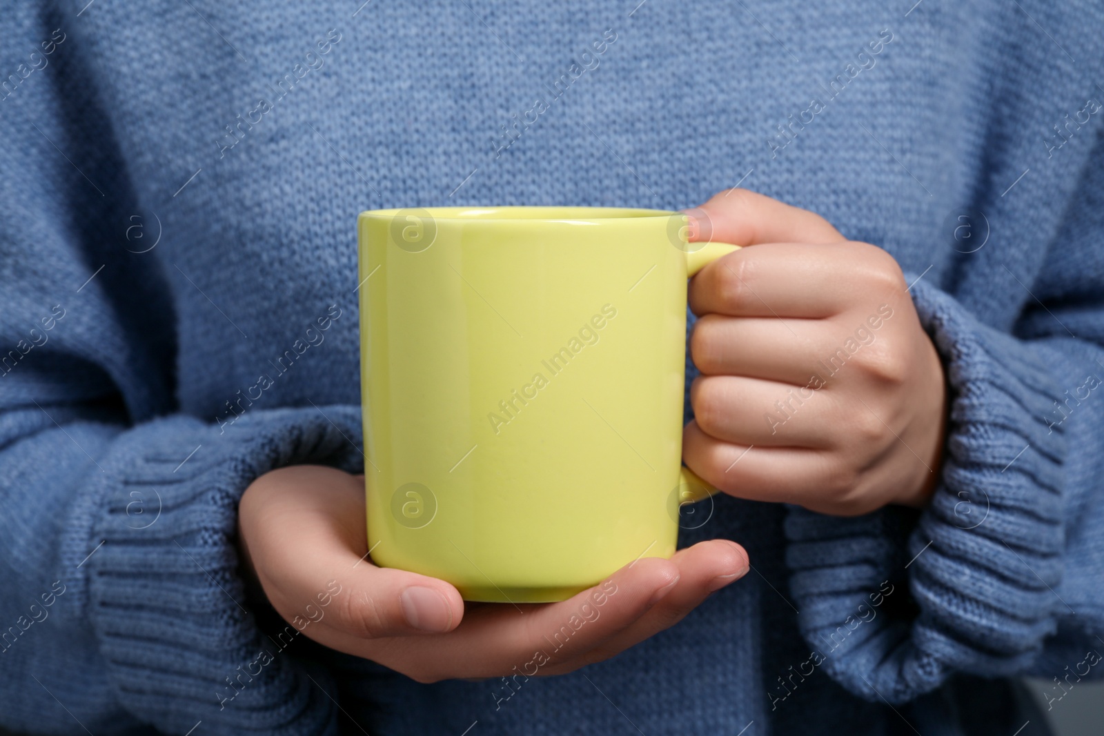 Photo of Woman holding yellow mug of drink, closeup