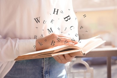 Image of Woman reading book with letters flying over it outdoors on sunny day, closeup