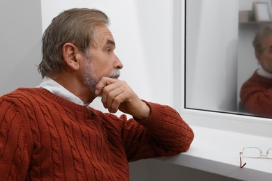 Photo of Upset senior man looking at window indoors. Loneliness concept