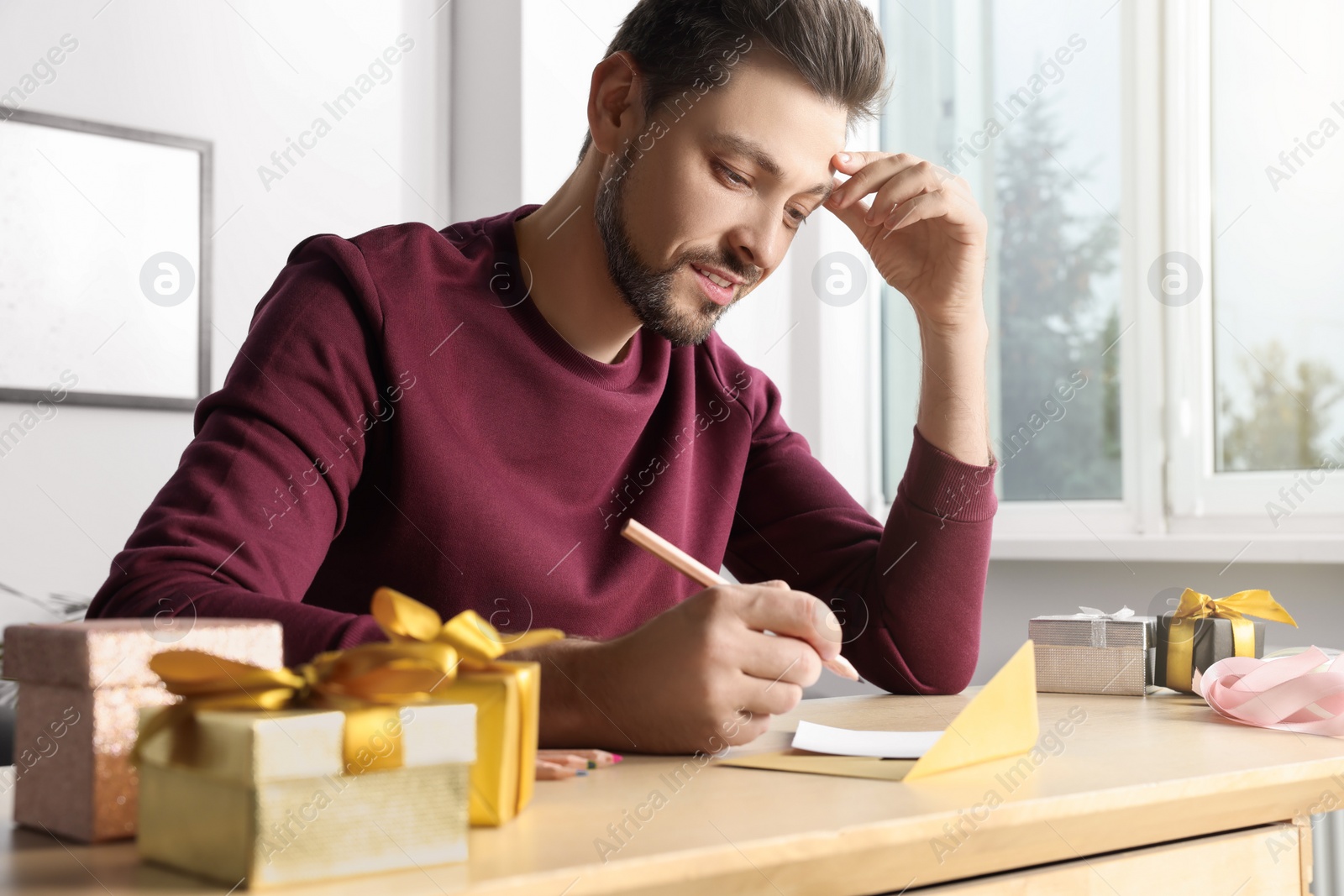 Photo of Man writing message in greeting card at wooden table in room