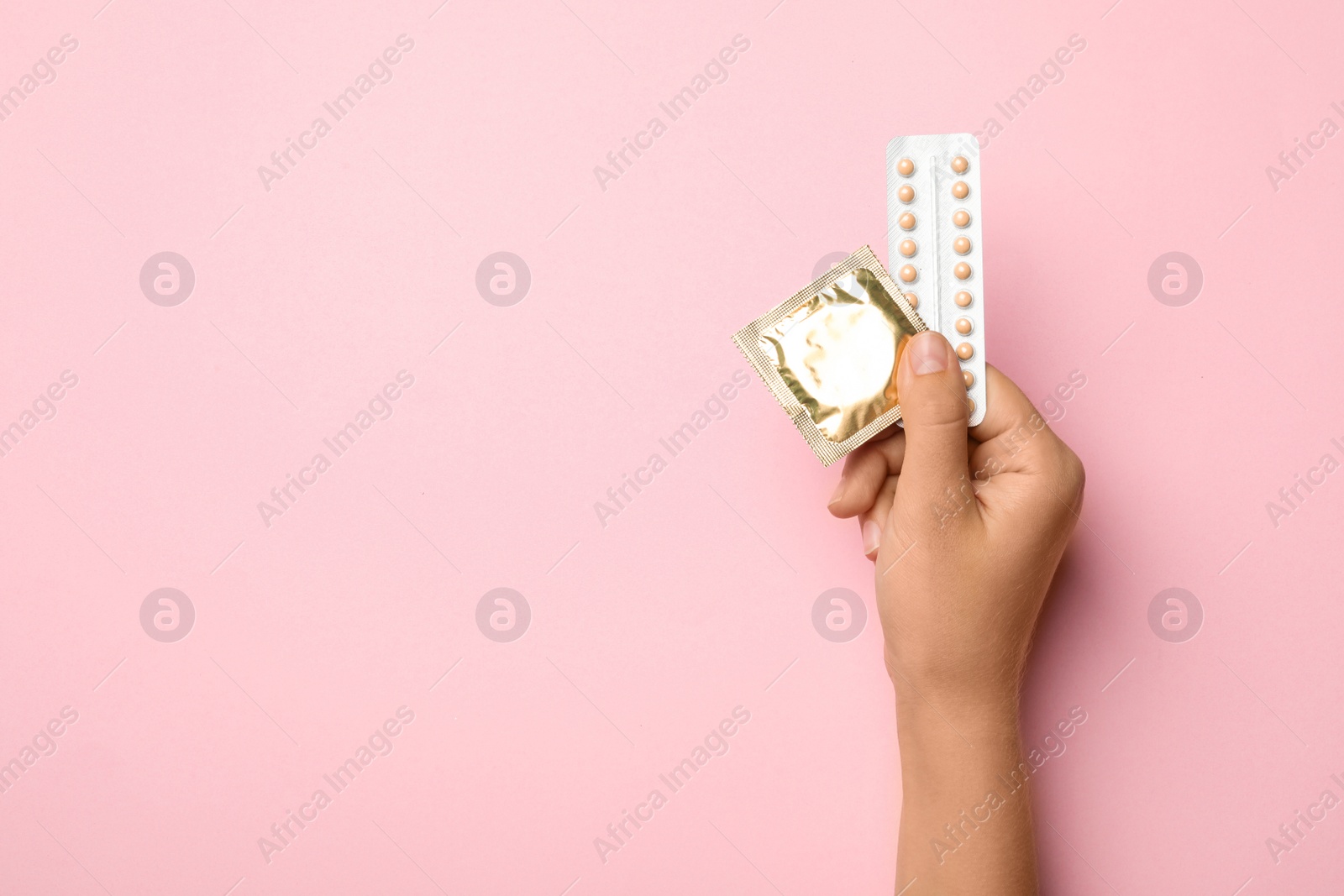 Photo of Woman holding condom and birth control pills on pink background, top view with space for text. Safe sex