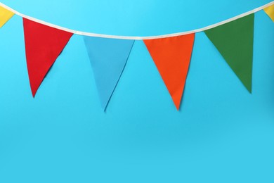 Bunting with colorful triangular flags on light blue background. Space for text