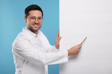 Photo of Ophthalmologist pointing at blank banner on light blue background, space for text