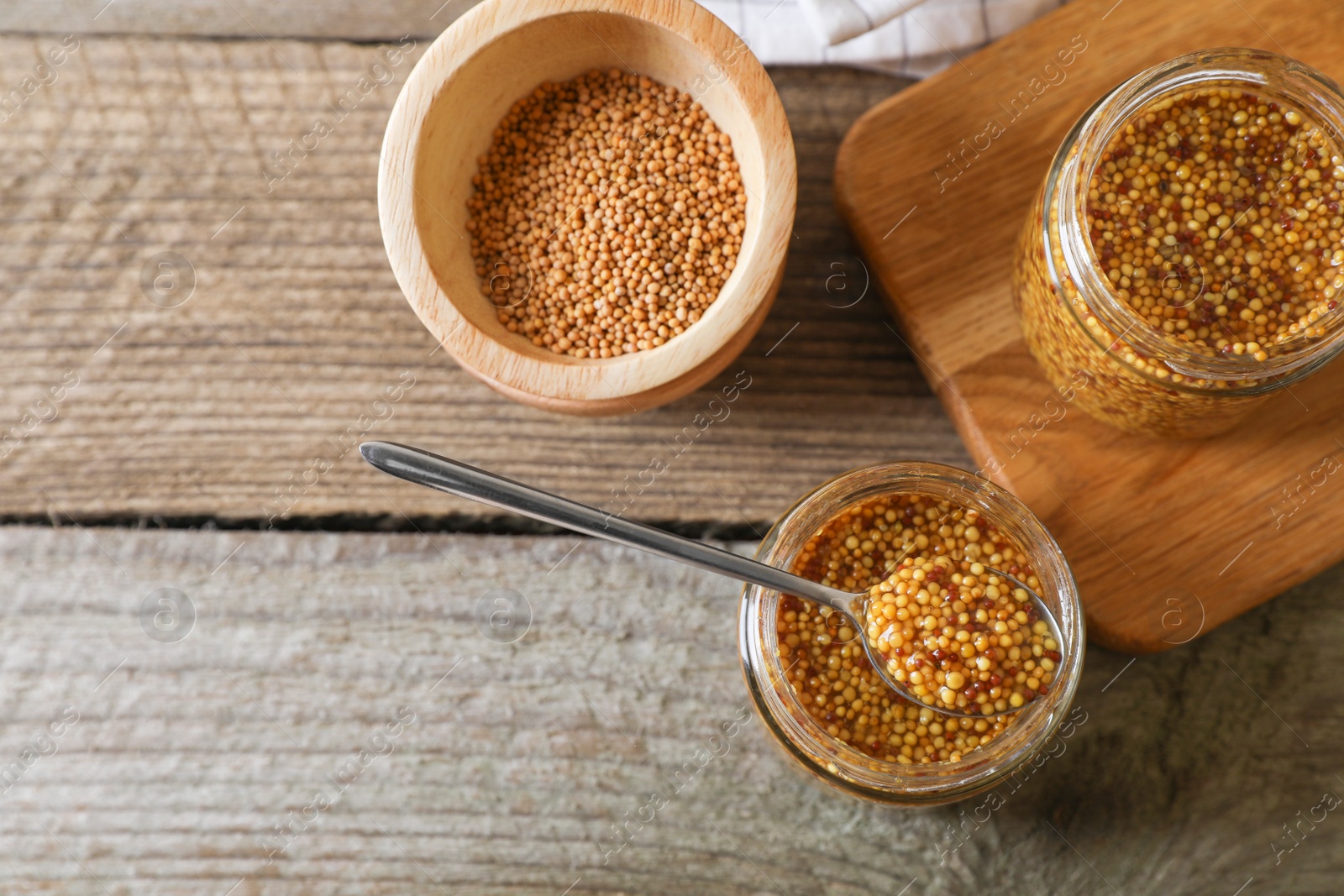 Photo of Bowl and jars of whole grain mustard on wooden table, flat lay. Space for text