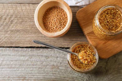 Photo of Bowl and jars of whole grain mustard on wooden table, flat lay. Space for text