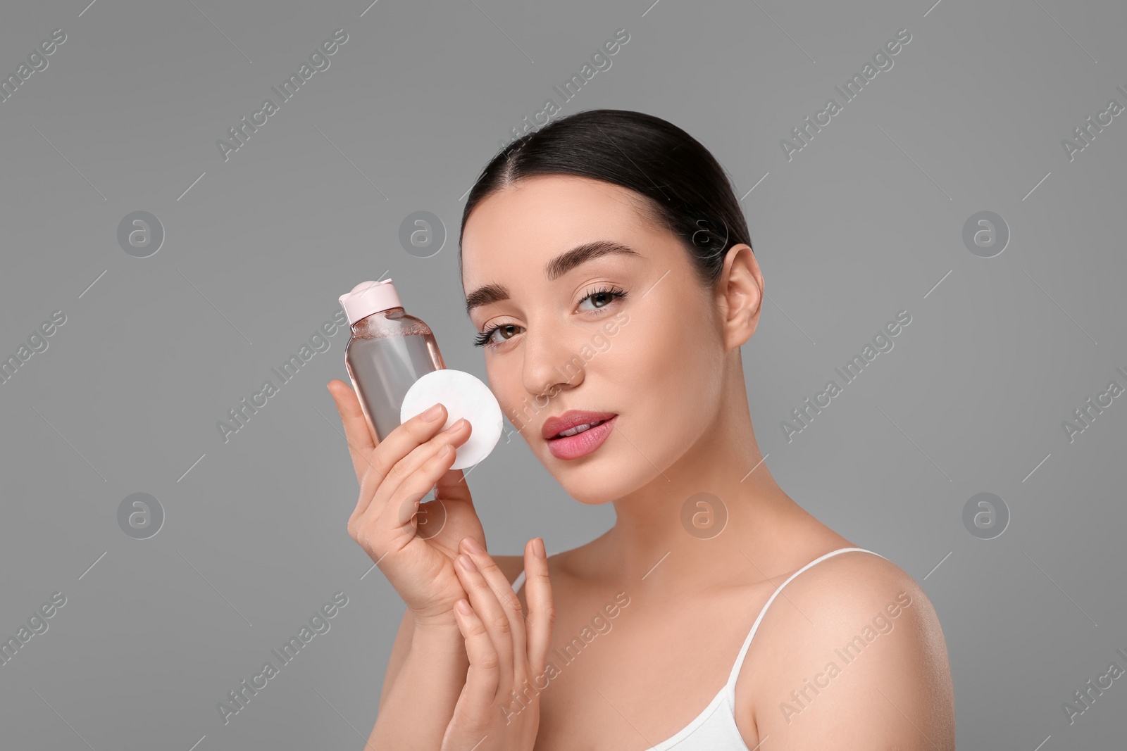 Photo of Beautiful woman with makeup remover and cotton pad on gray background