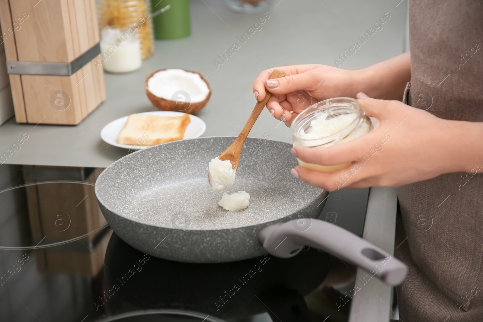 Photo of Woman putting coconut oil on frying pan in kitchen, closeup