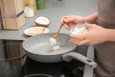 Woman putting coconut oil on frying pan in kitchen, closeup