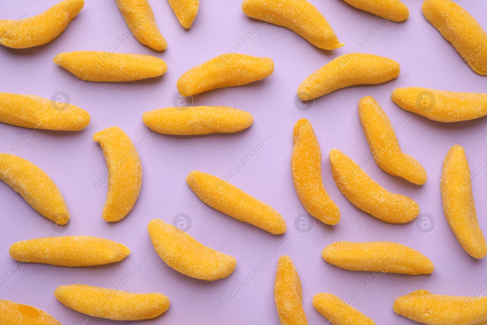 Photo of Tasty jelly candies in shape of banana on lilac background, flat lay