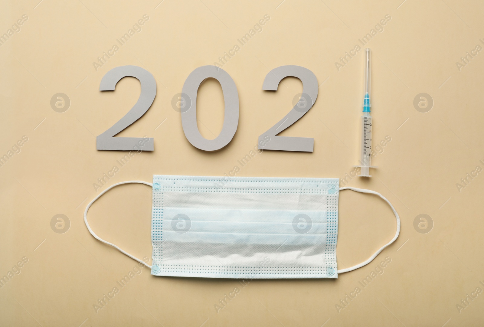 Photo of Paper numbers with syringe forming 2021 and medical mask on beige background, flat lay. Coronavirus vaccination