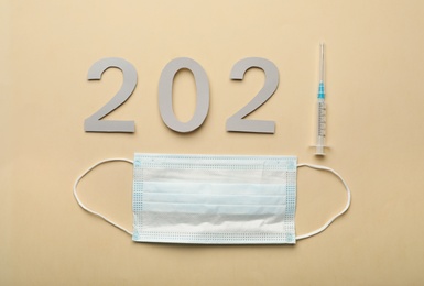 Photo of Paper numbers with syringe forming 2021 and medical mask on beige background, flat lay. Coronavirus vaccination