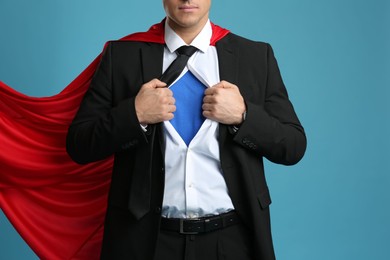 Businessman in superhero cape taking suit off on light blue background, closeup