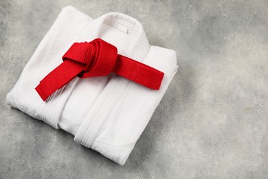 Red karate belt and white kimono on gray textured background, top view. Space for text