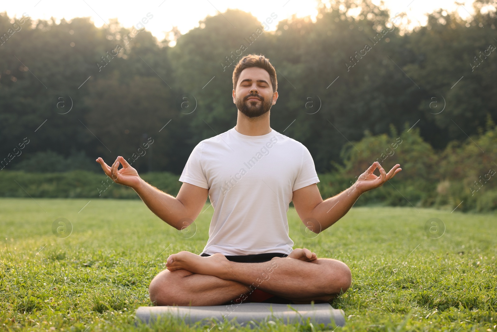 Photo of Man practicing yoga on mat outdoors. Lotus pose