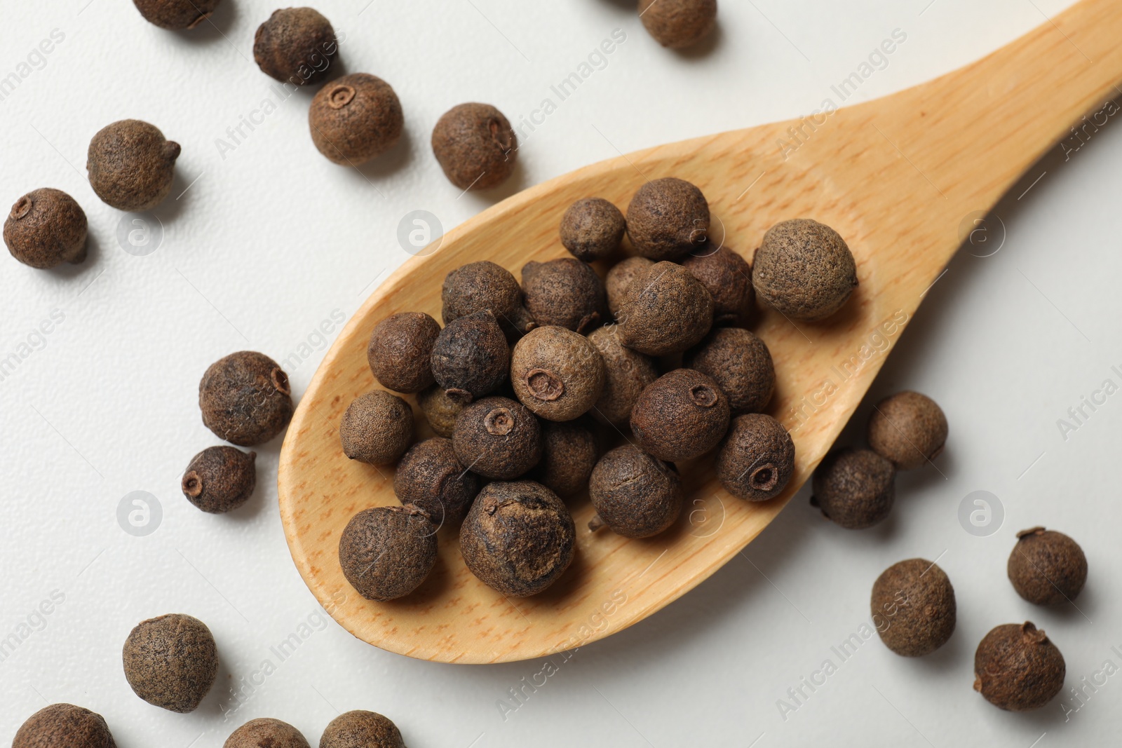 Photo of Dry allspice berries (Jamaica pepper) and spoon on white marble table, top view