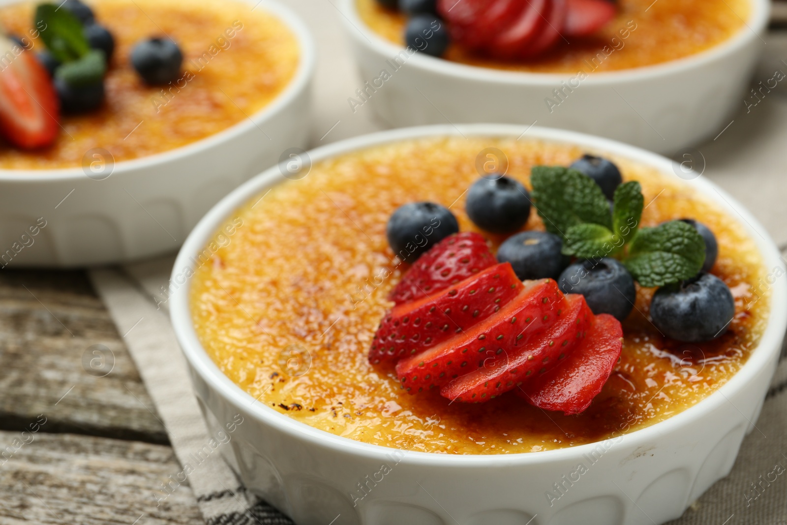 Photo of Delicious creme brulee with berries and mint in bowls on wooden table, closeup