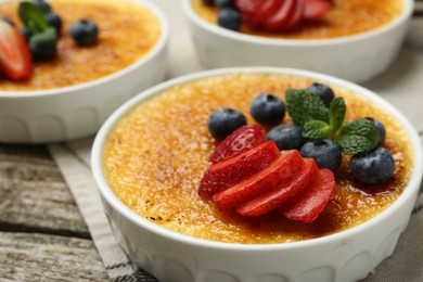 Delicious creme brulee with berries and mint in bowls on wooden table, closeup