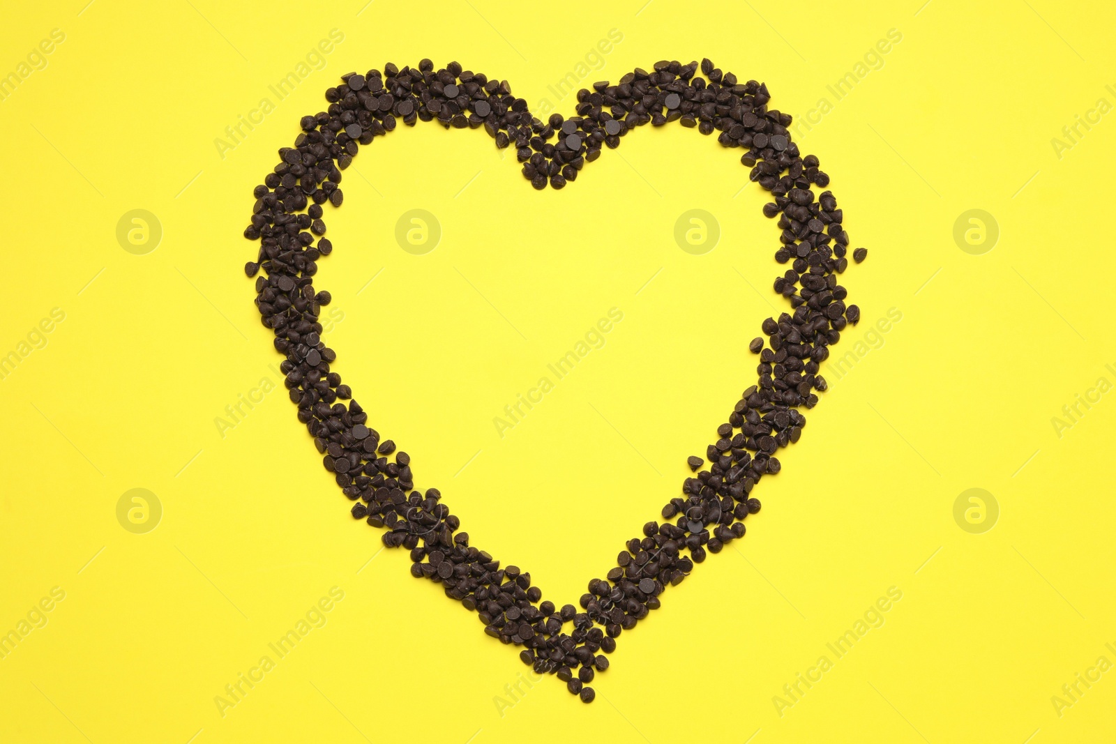 Photo of Heart made of delicious chocolate chips on yellow background, top view. Space for text