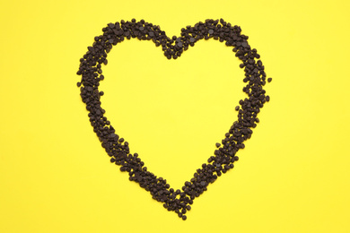 Photo of Heart made of delicious chocolate chips on yellow background, top view. Space for text