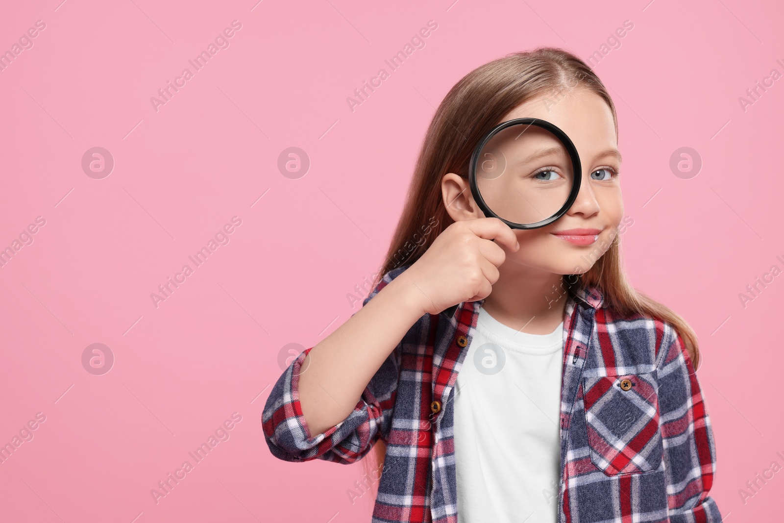 Photo of Cute little girl looking through magnifier on pink background, space for text