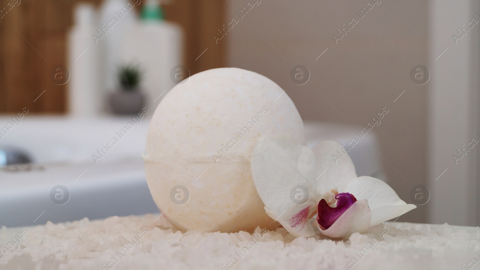 Photo of Bath bomb with orchid and sea salt on table in bathroom, closeup