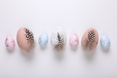 Photo of Many painted Easter eggs with feathers on white background, flat lay