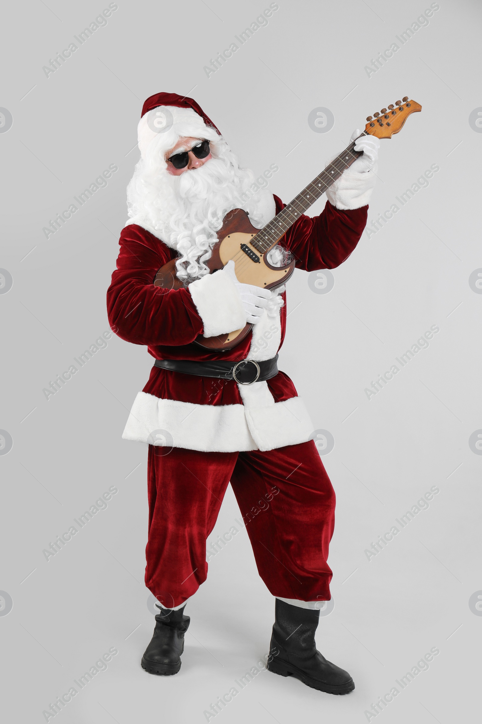 Photo of Santa Claus playing electric guitar on light grey background. Christmas music