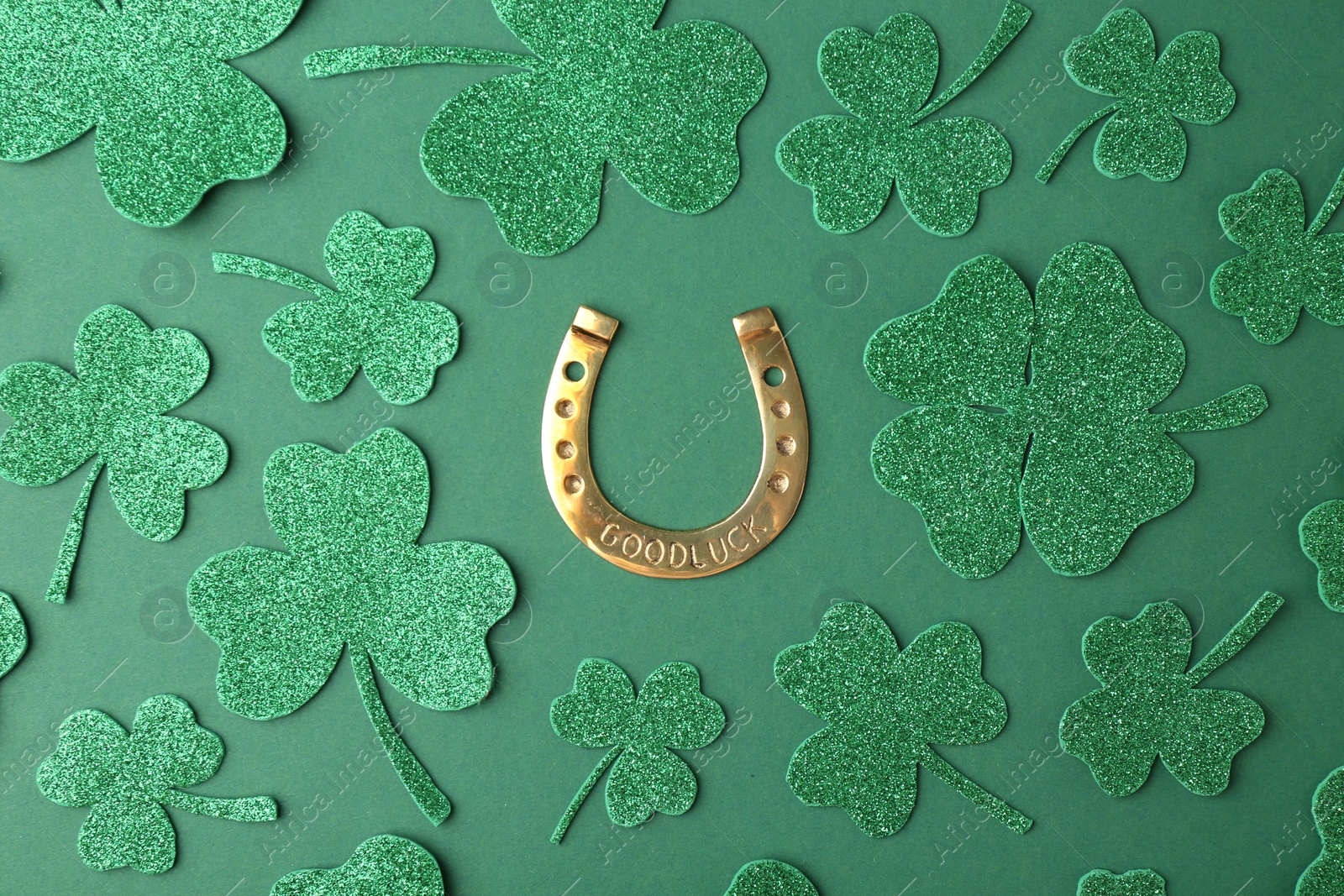 Photo of St. Patrick's day. Golden horseshoe and decorative clover leaves on green background, flat lay